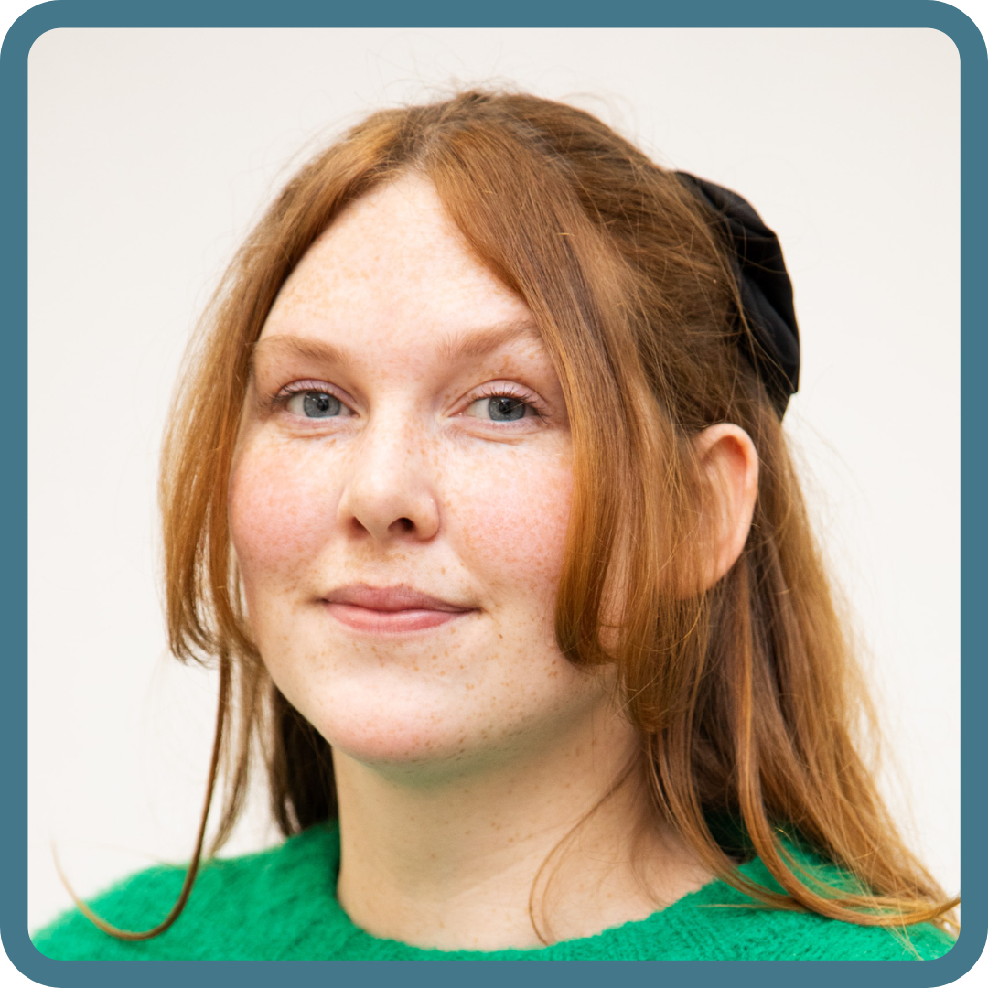 Woman with ginger hair tied back looks to camera and smiles.