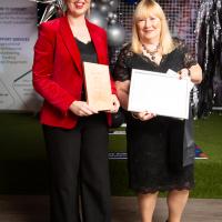 Two women stand with award smiling. Gear Up, Enterprise and Sustainability award.