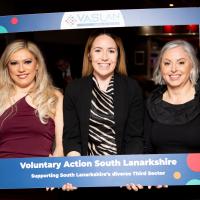 Three women smile in large photo frame. 