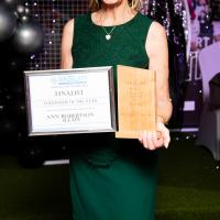 Woman in green dress smiles with award. Anne Robertson, LEAP, volunteer of the year. 