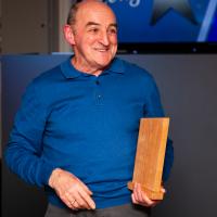 Man in blue shirt smiles with wooden award. Burnbank community hub. 