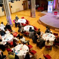 Overhead shot of tables, chairs and people facing towards a stage. 