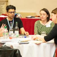 Group of 6 people in mid discussion around a table. 