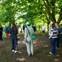 Group of people stand in a circle having a conversation in the middle of a forest. 
