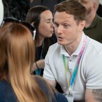 Two people are seen mid-discussion sitting down. 