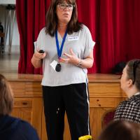 Woman with brown hair and grey t-shirt presents to the room. 