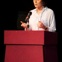 Woman stands at a red podium giving a speech to the room. 