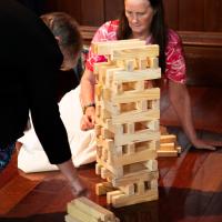 Two women concentrate as they play a large jenga game on a wooden floor. 