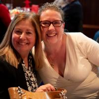 Two women smile facing the camera as they enjoy the event. 