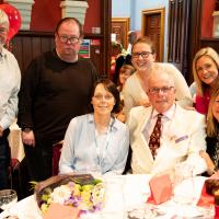 Group of people sit around a table, smiling at the camera.  