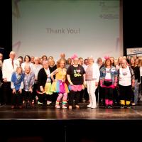 Large group of people stand on stage in front of a large screen reading "Thank You"